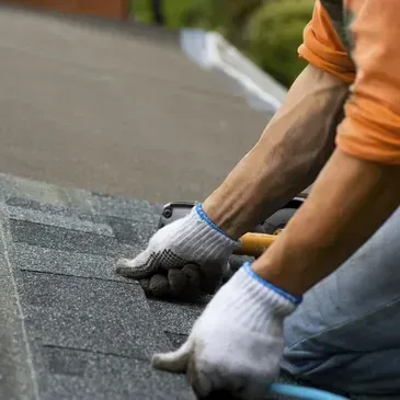 Roofer in gloves installing shingles on a roof